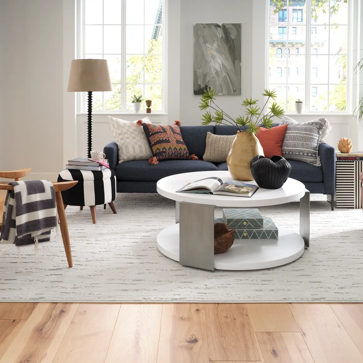 Modern living room with light wood flooring, featuring a navy sofa, colorful cushions, and a white round coffee table